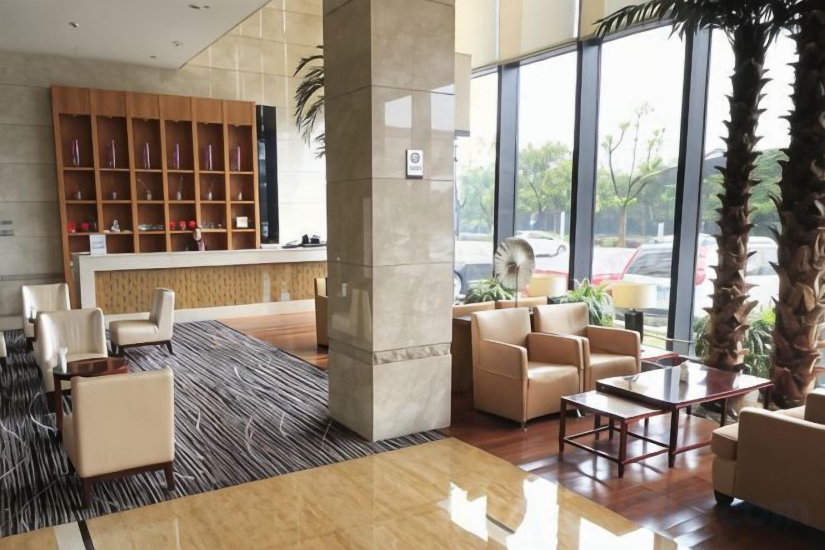 A hotel lobby with a reception desk, seating area, and large windows.