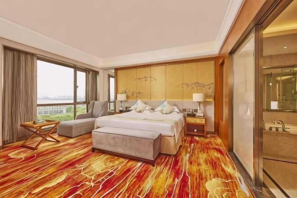 A hotel room with a bed, a sofa, a nightstand, a lamp, and a large window with a view.