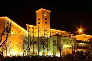 Un hotel de varios pisos con una torre destacada, fachada de vidrio y una entrada bien iluminada.