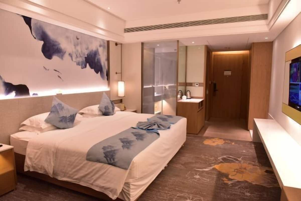 A modern hotel room with a large bed, a bathroom with a mirror and sink, and a TV on the wall.