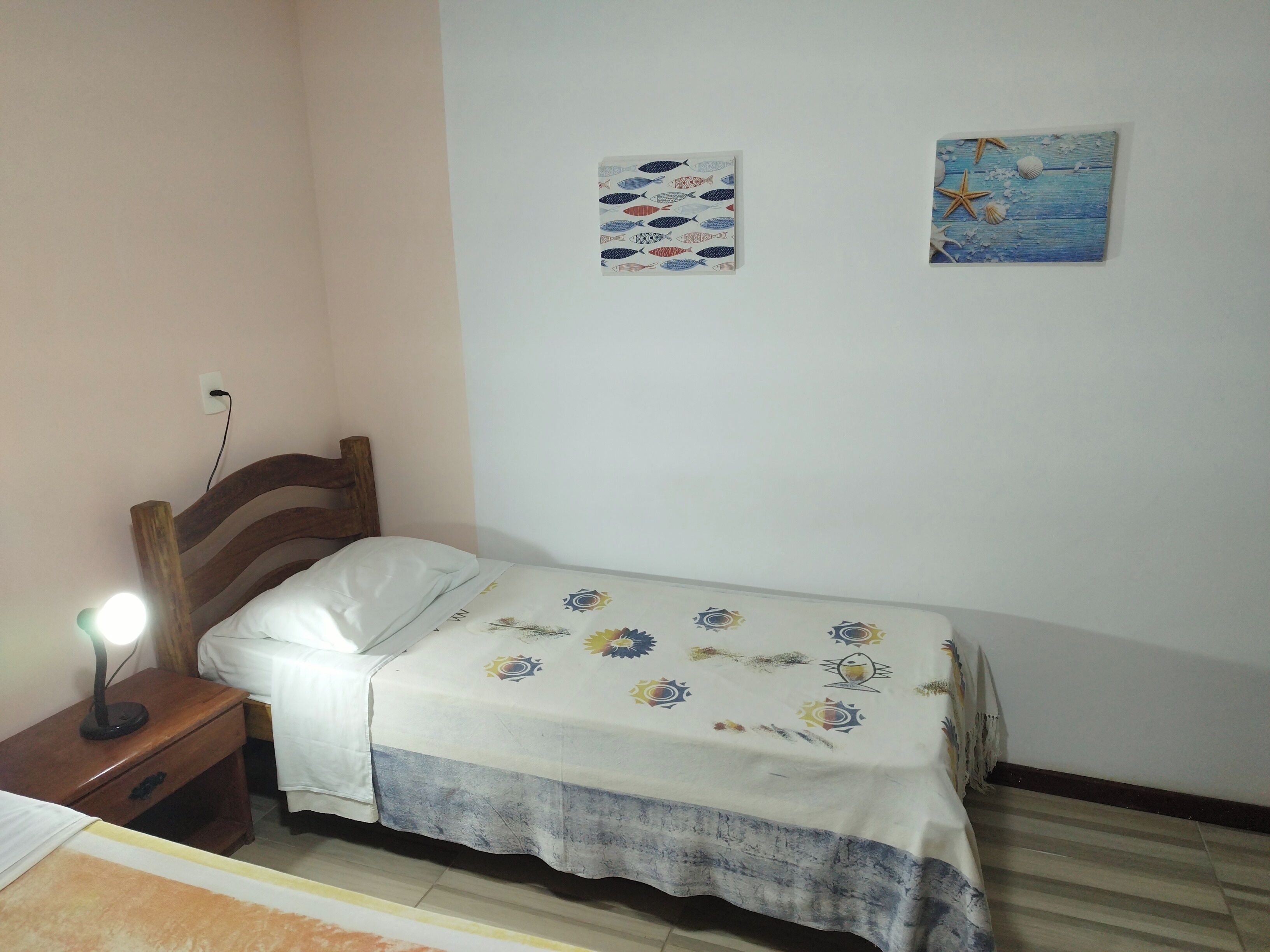 A bedroom with a wooden headboard, a bedside table with a lamp, a bed with a floral bedspread, and two wall-mounted pictures.