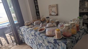 Een ontbijtbuffet met diverse etenswaren en drankjes, een houten vloer en uitzicht op buiten.