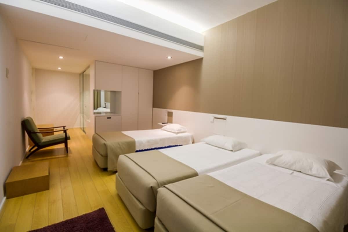 A hotel room with two beds, a chair, and a small desk.