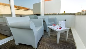 A balcony with two white sofas, a small table with a bottle and glasses, and a view of buildings in the background.