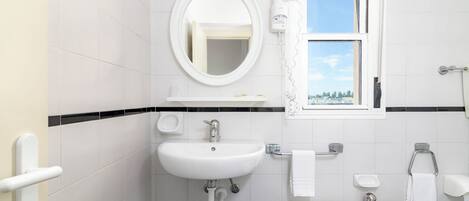 A modern bathroom with a white sink, round mirror, and a window with a view of the outside.