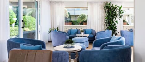 A modern living room with blue armchairs, a white coffee table, and a large window with curtains.