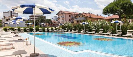 A swimming pool with sun-shaped tiles, lounge chairs, and umbrellas.