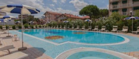 Una piscina con sillas de descanso y sombrillas, rodeada de edificios.