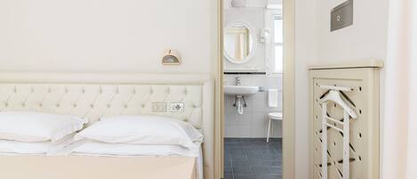 A bedroom with a bed, a bedside table, a mirror, and a bathroom visible through an open door.