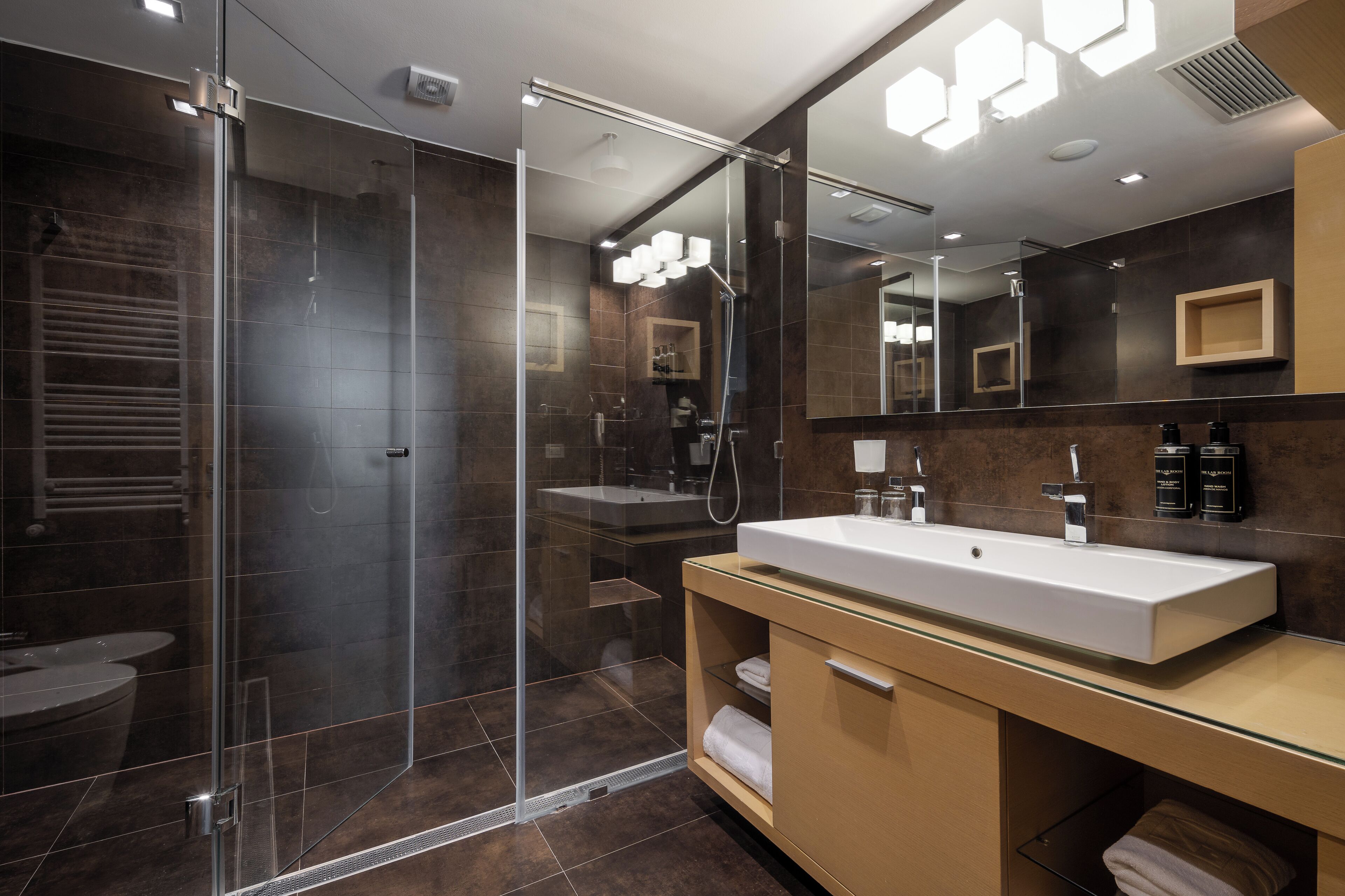 Une salle de bain moderne avec une douche à parois de verre, un grand miroir et un meuble-lavabo avec un évier blanc.