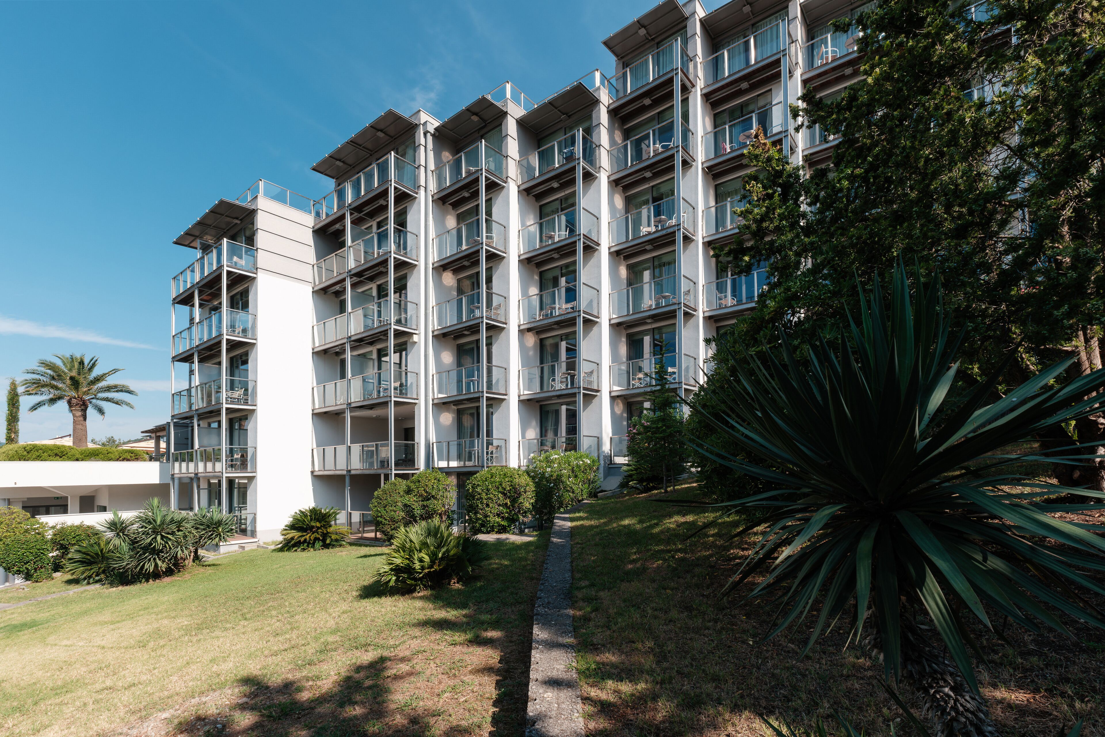 Un hotel moderno de varios pisos con balcones, césped cuidado y jardines tropicales.