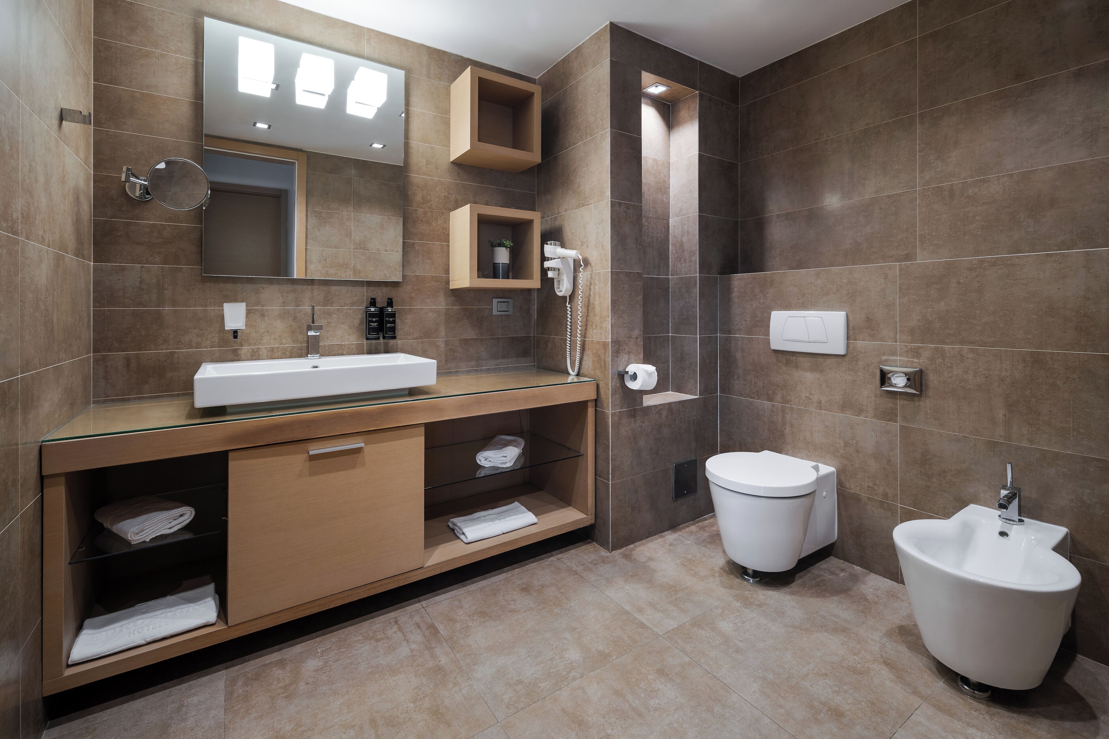 Een moderne badkamer met een glazen wastafel, toilet, bidet en grote spiegel.