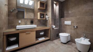Een moderne badkamer met een glazen wastafel, toilet, bidet en grote spiegel.