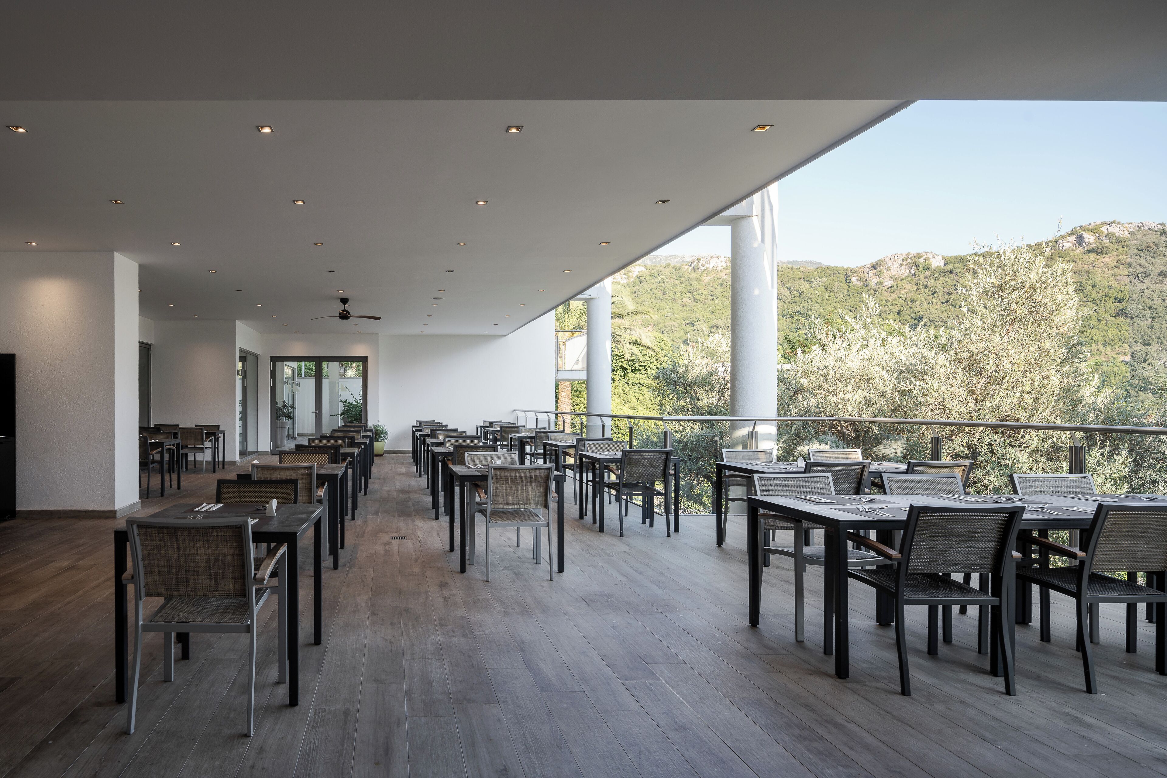 A spacious outdoor dining area with multiple tables and chairs, large windows, and a view of a mountainous landscape.