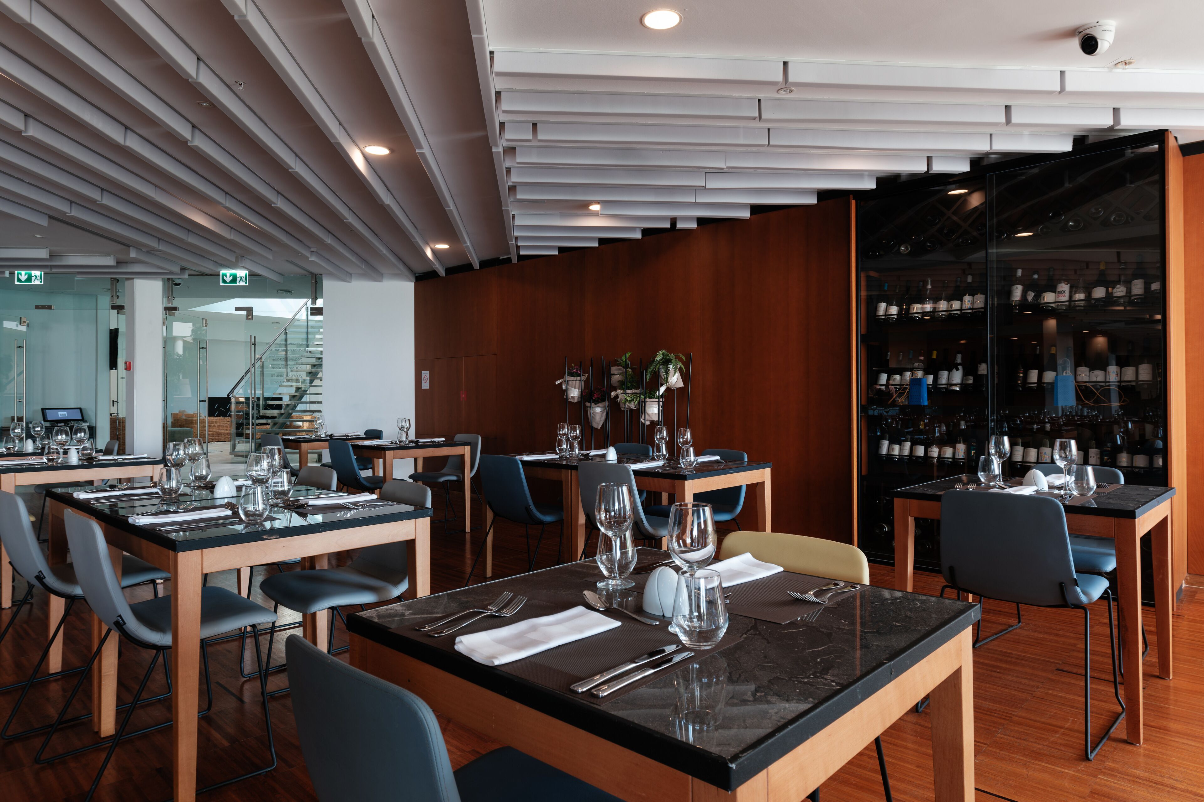 En moderne restaurant med glasvægge, træborde og blå stole.