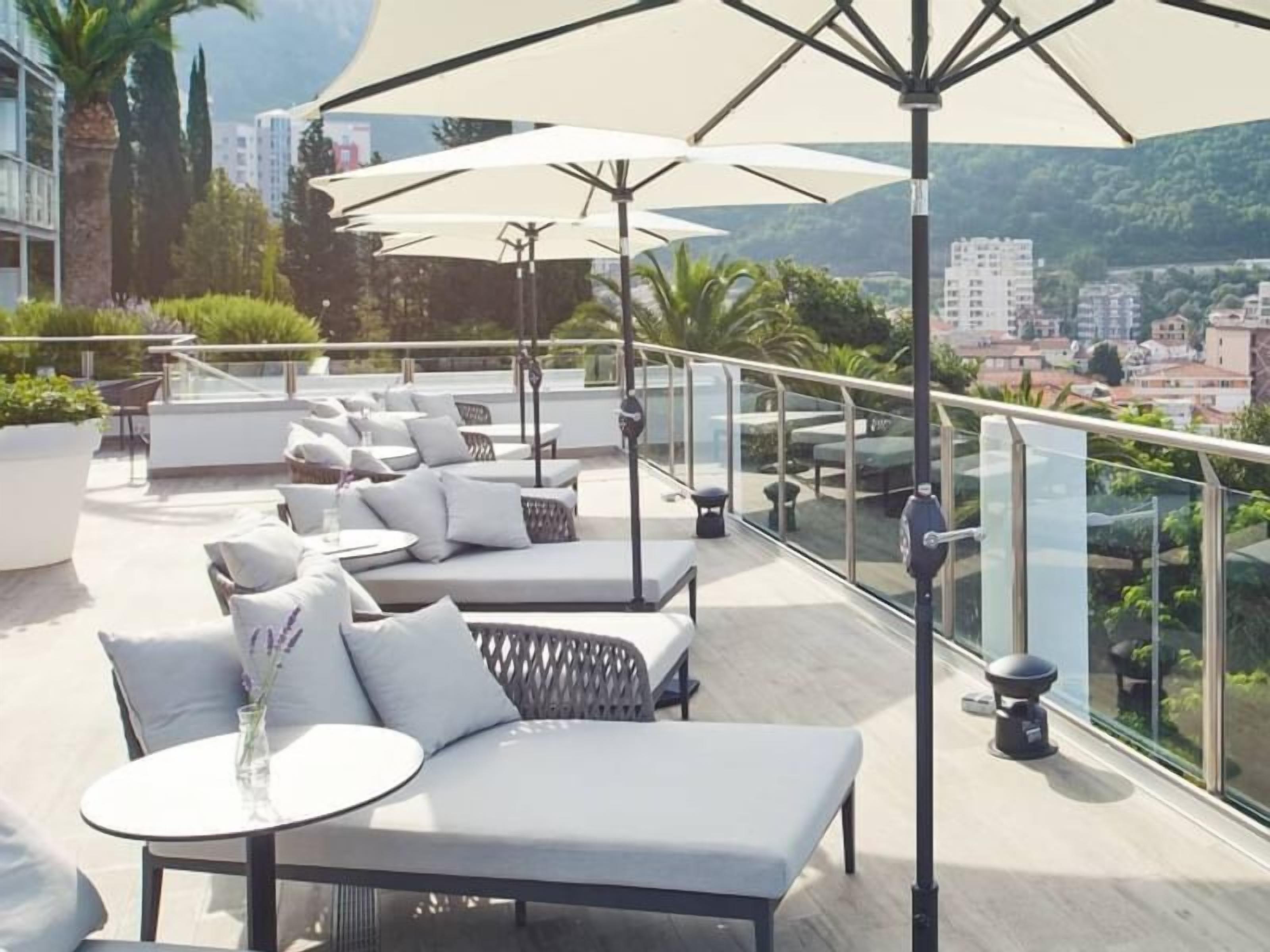 Une terrasse sur le toit, aménagée avec des espaces de détente en plein air, comprenant des canapés et des tables, ainsi que des parasols pour créer de l’ombre.