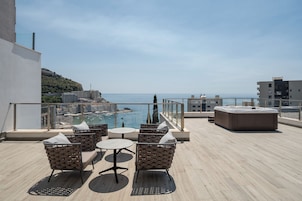 Terraza en la azotea con mobiliario exterior, jacuzzi y vistas al mar y al paisaje urbano.