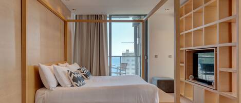 A modern hotel room with a large bed, a TV on a wooden shelf, and a balcony with a view of the city.
