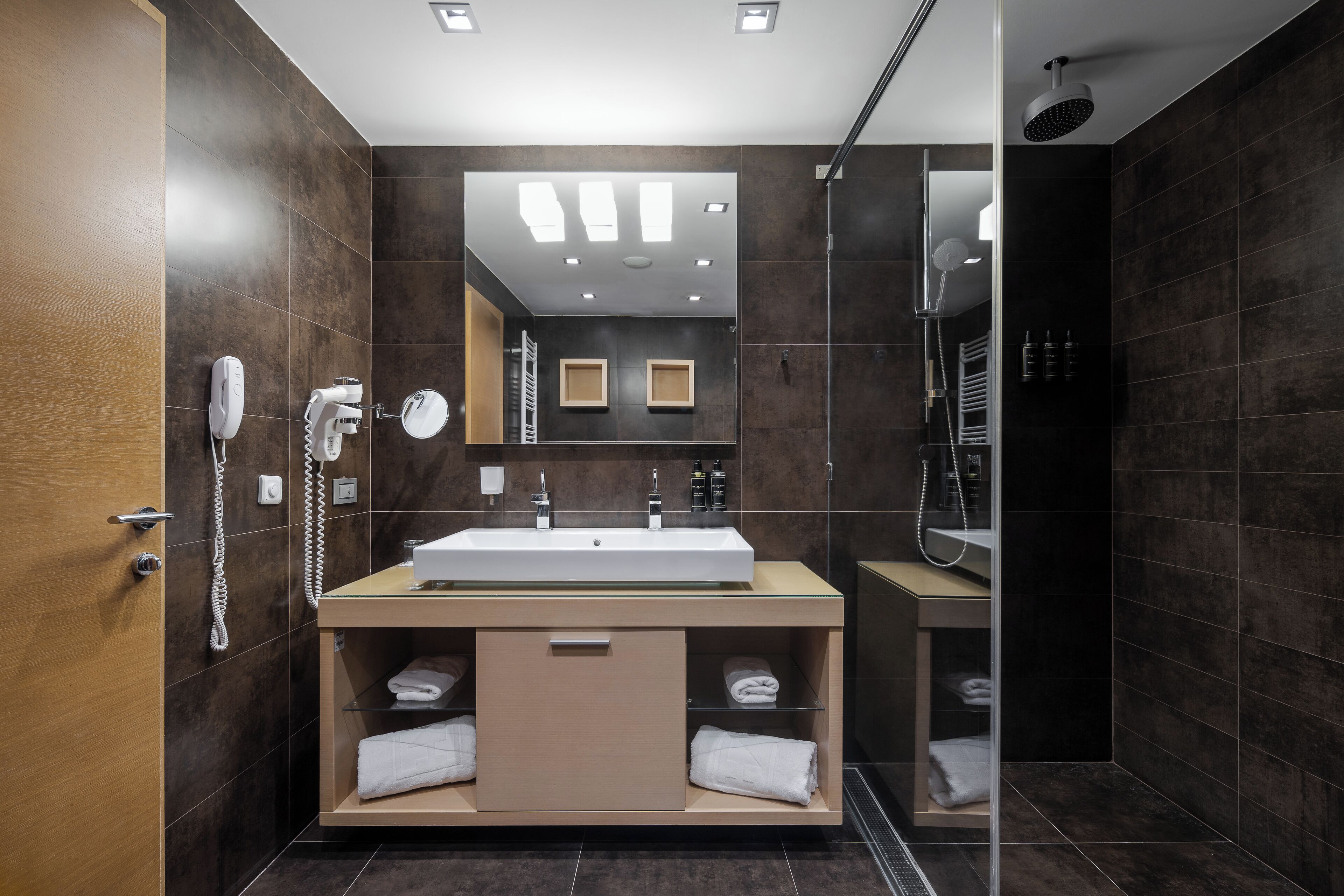 A modern bathroom with a large mirror, a sink, a shower, and a toilet.