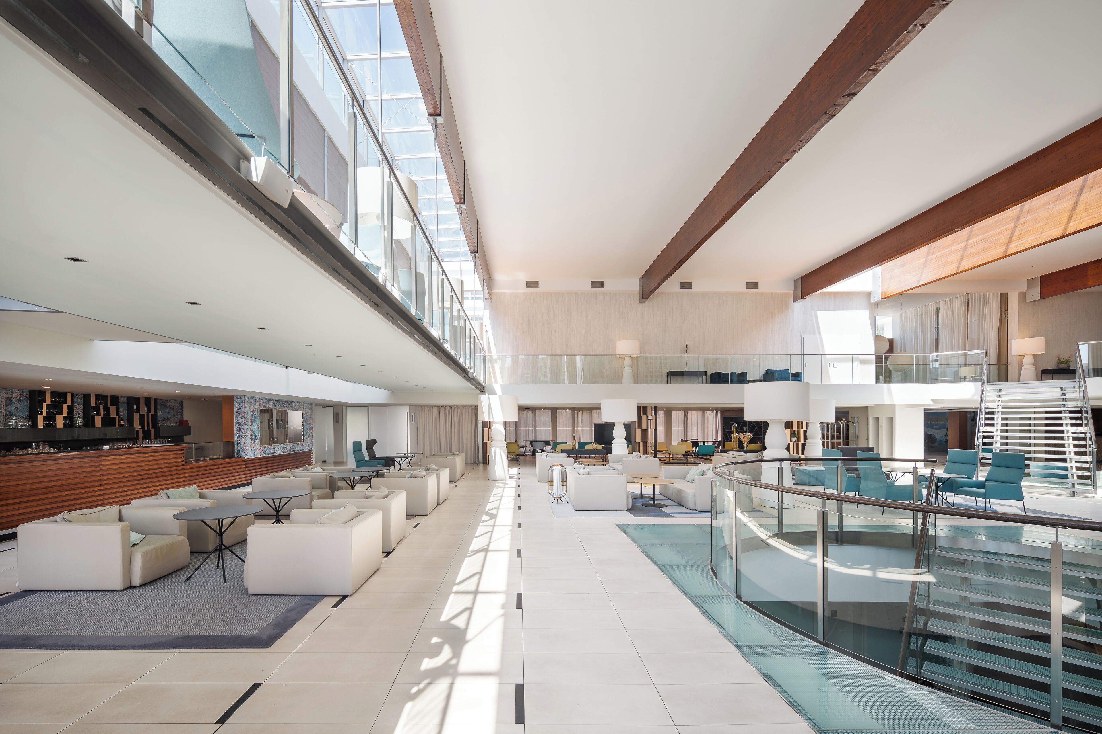 A spacious, modern lobby with a glass railing, multiple seating areas, and a visible staircase.