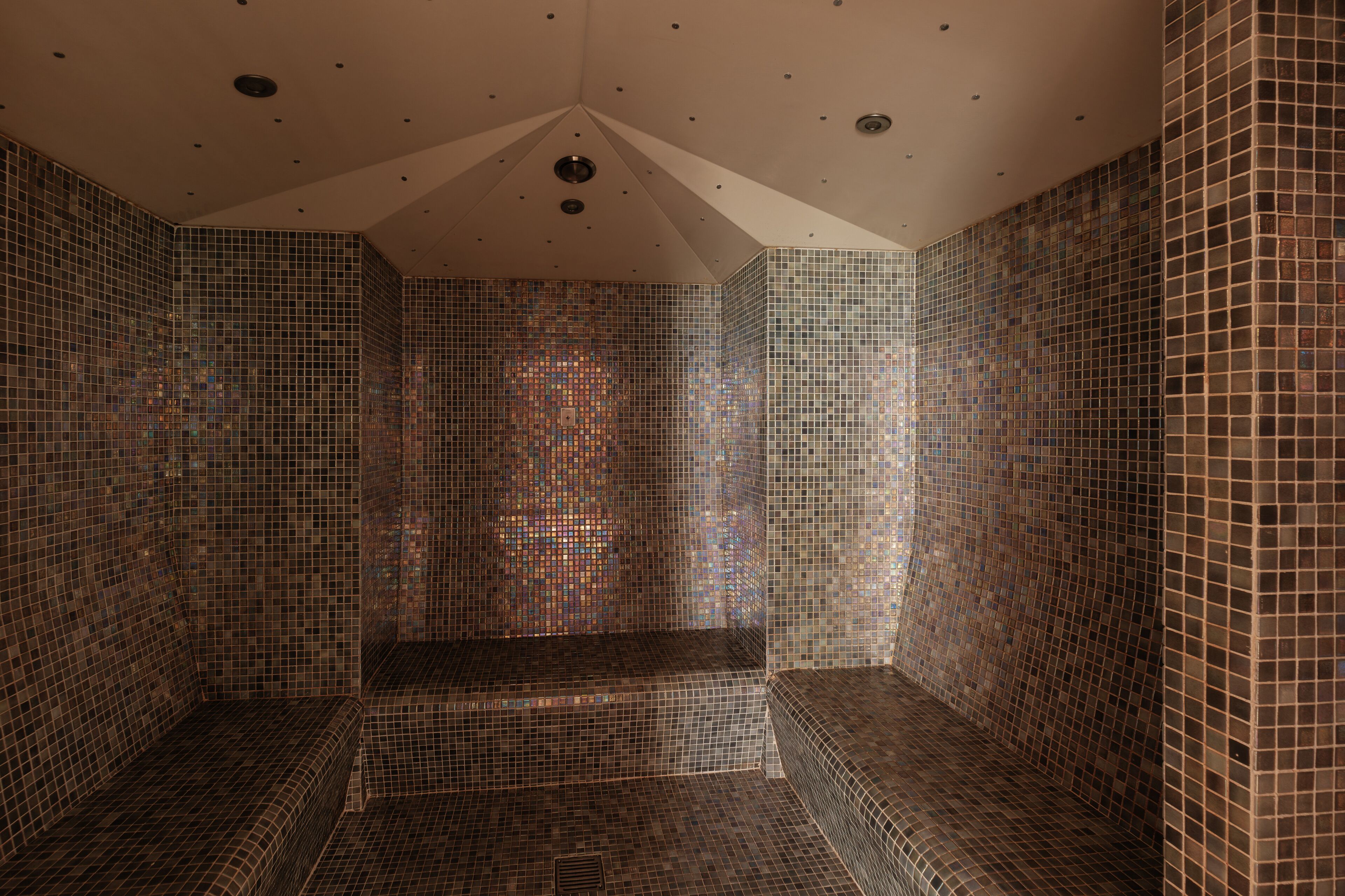 A room with mosaic tiled walls and a bench.