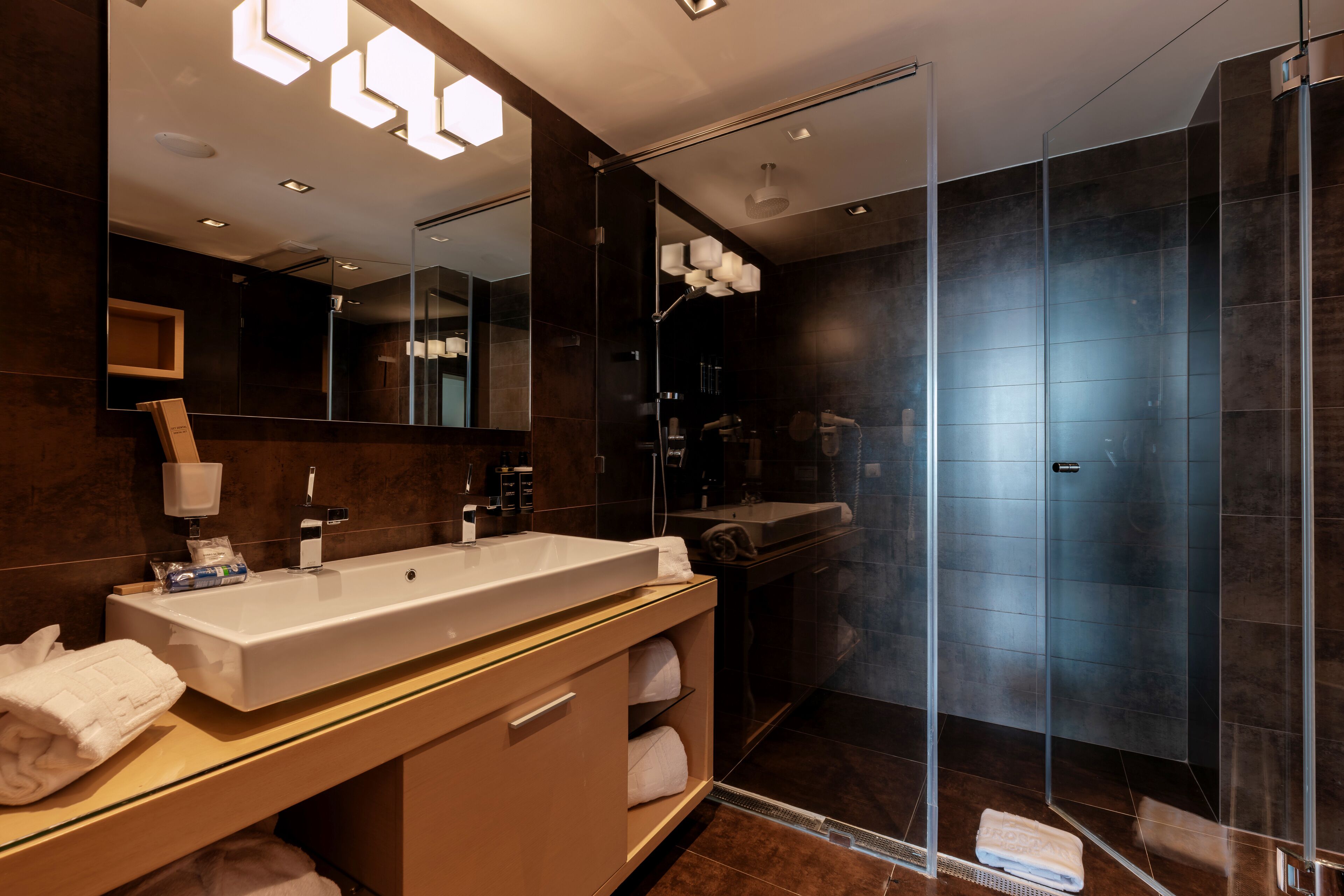 Een moderne badkamer met een grote spiegel, een wit wastafelmeubel en een douche met glazen wanden.