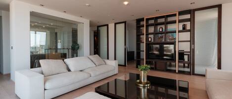 A modern living room with a white sofa, a glass coffee table, and a television on a wooden stand.