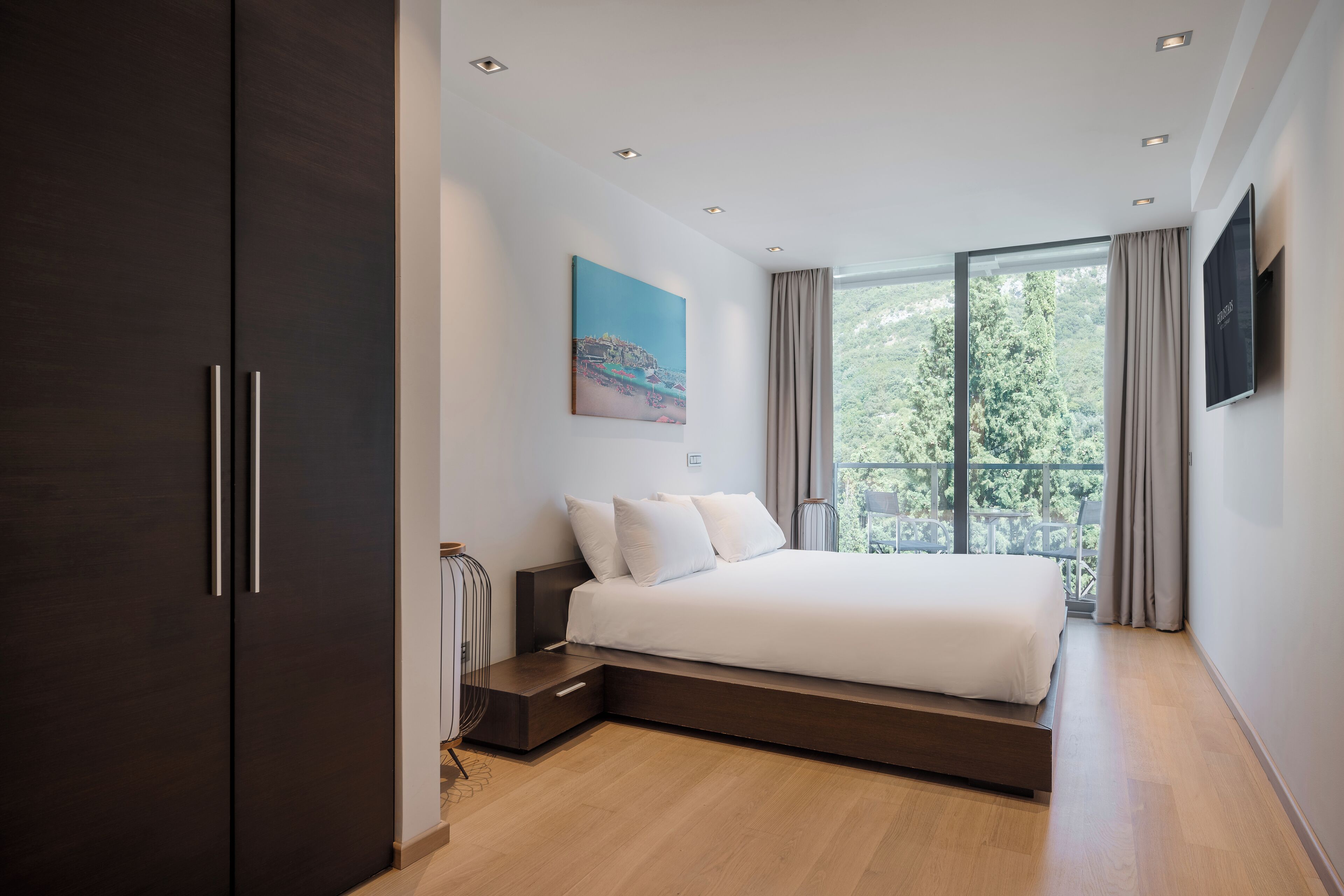Ein modernes Schlafzimmer mit einem großen Bett, einem Nachttisch, einem dunklen Kleiderschrank, einem Gemälde und einem großen Fenster mit Vorhängen.