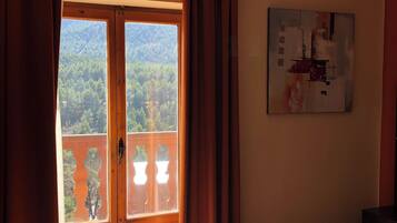 Habitación de hotel con una puerta de madera grande que da a un balcón, una cama con colcha estampada y un cuadro en la pared.