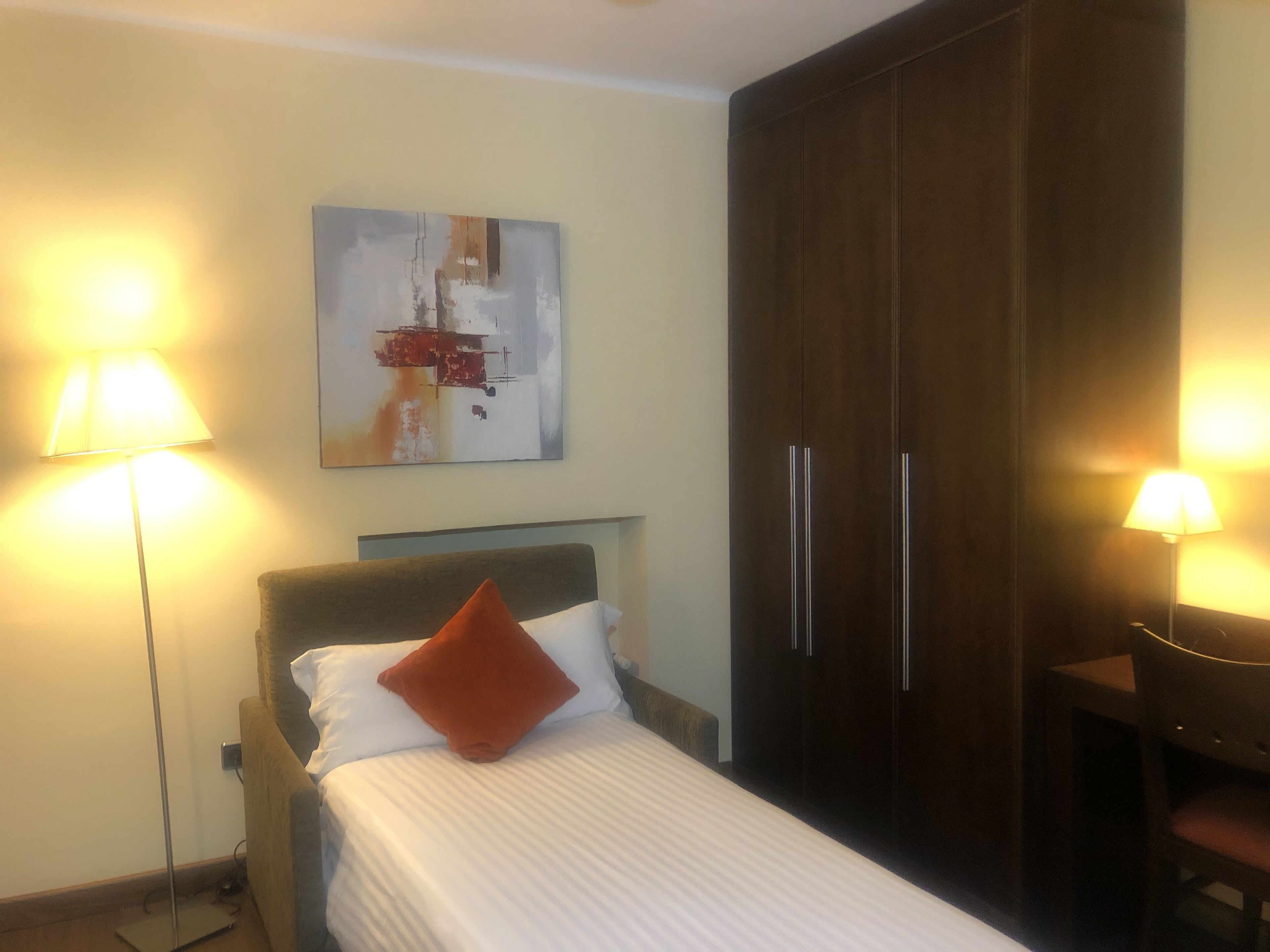 Une chambre d’hôtel avec un lit, une armoire et deux lampadaires.