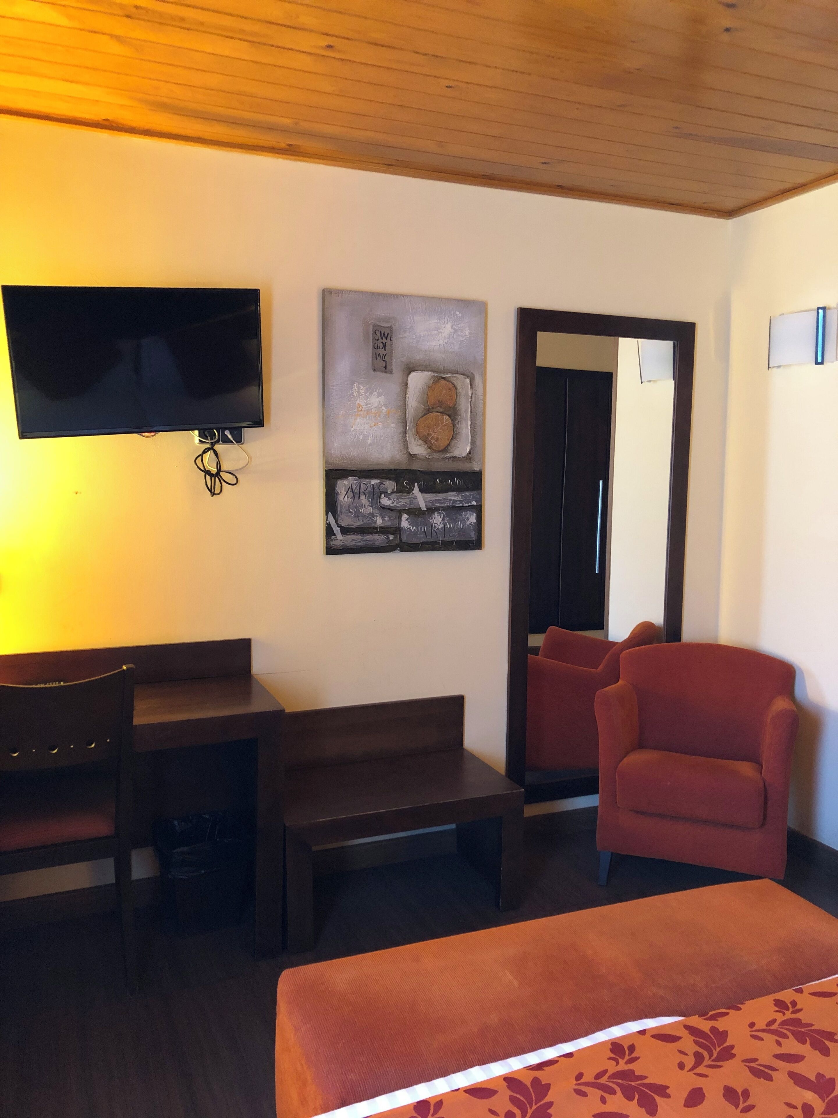 Quarto de hotel com cama, escrivaninha, cadeira, televisão e um quadro na parede.