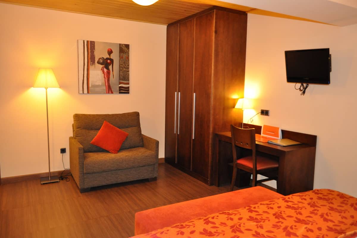A room with a sofa, a desk, a chair, a bed, a wardrobe, and a television.