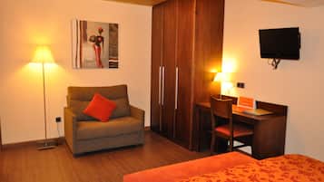 A room with a sofa, a desk, a chair, a bed, a wardrobe, a television, and a painting on the wall.