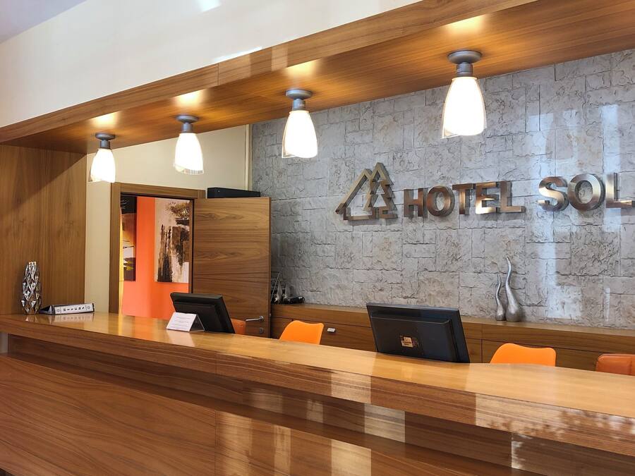 A hotel reception desk with a wooden counter, three pendant lights, and a stone-textured wall with the hotel's name.