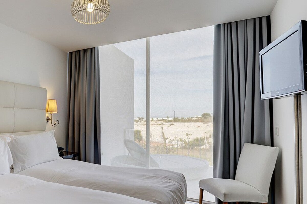 A hotel room with a large bed, two bedside lamps, a TV, and a view of the outdoors.