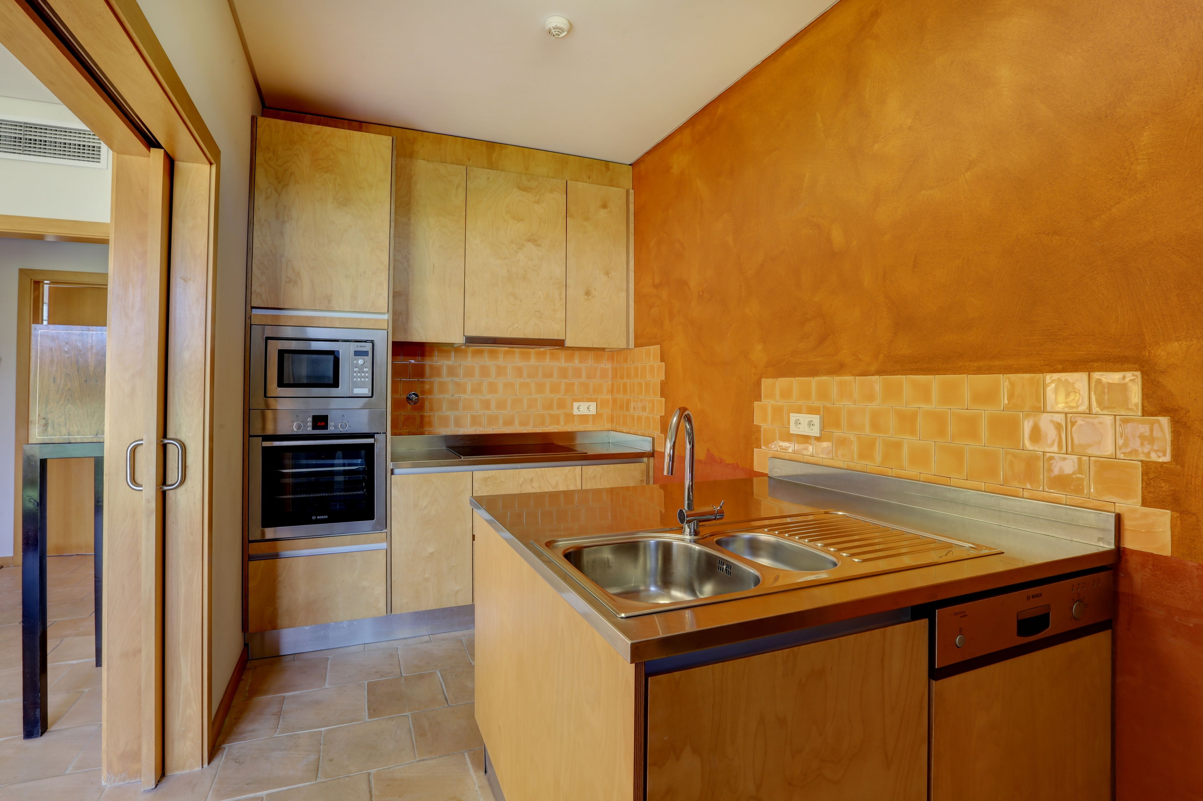 A compact kitchen with wooden cabinets, a built-in microwave, and a stainless steel sink.