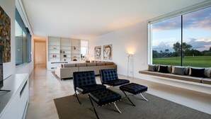Una sala de estar moderna con un ventanal grande, un sofá, dos sillones y una estantería.