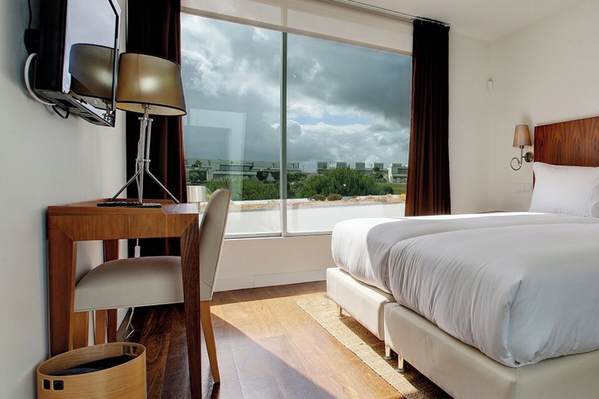 A hotel room with a bed, desk, chair, and a view of the cityscape.