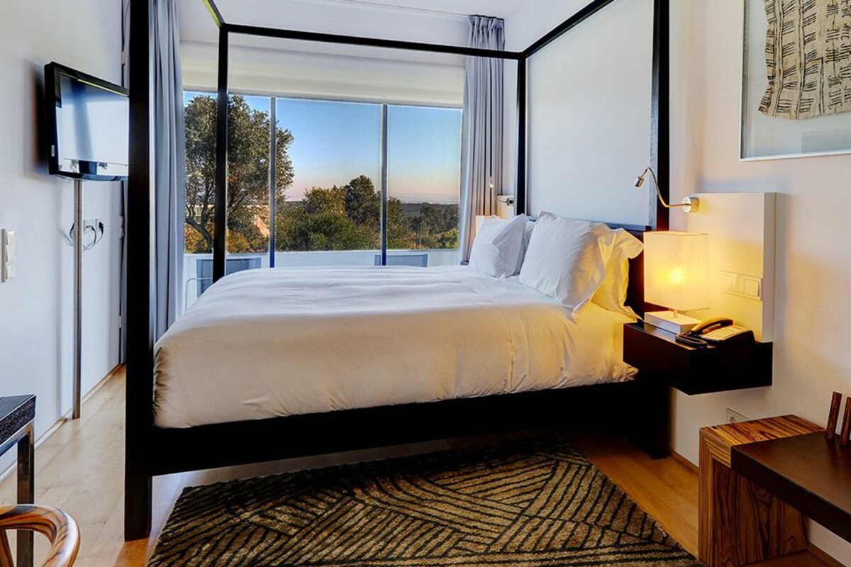 A modern bedroom with a bed, bedside table, lamp, and artwork.