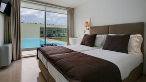 Una habitación de hotel con una cama grande, un televisor montado en la pared y vistas a una piscina por la ventana.
