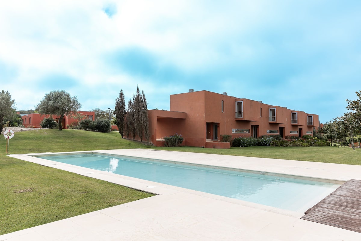 Un bâtiment moderne doté d’une piscine, entouré de pelouses et d’arbres bien entretenus.