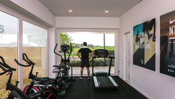 A gym with exercise equipment, a treadmill, and a person standing by the window.