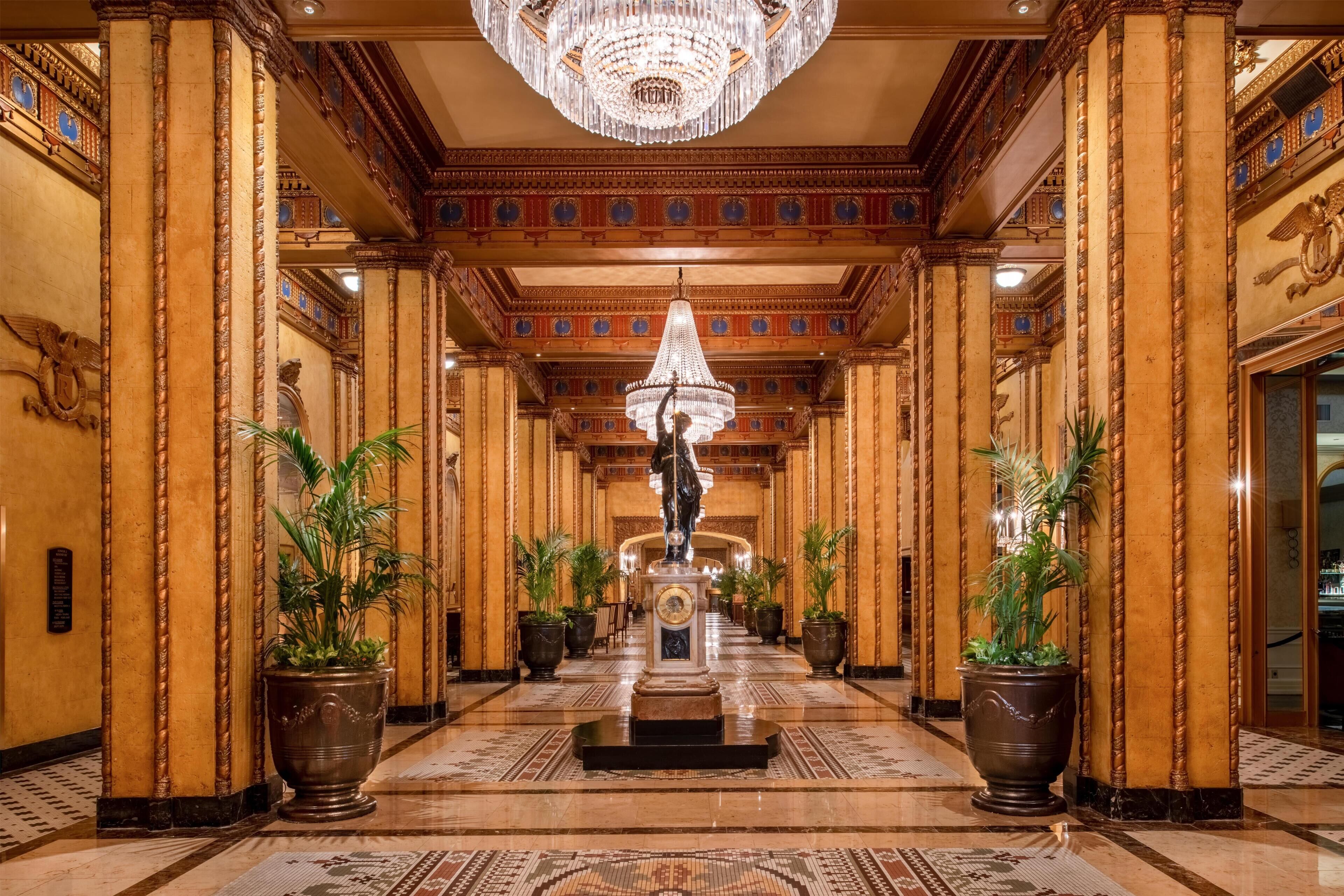 A grand hallway with ornate columns, a central statue, and a chandelier.