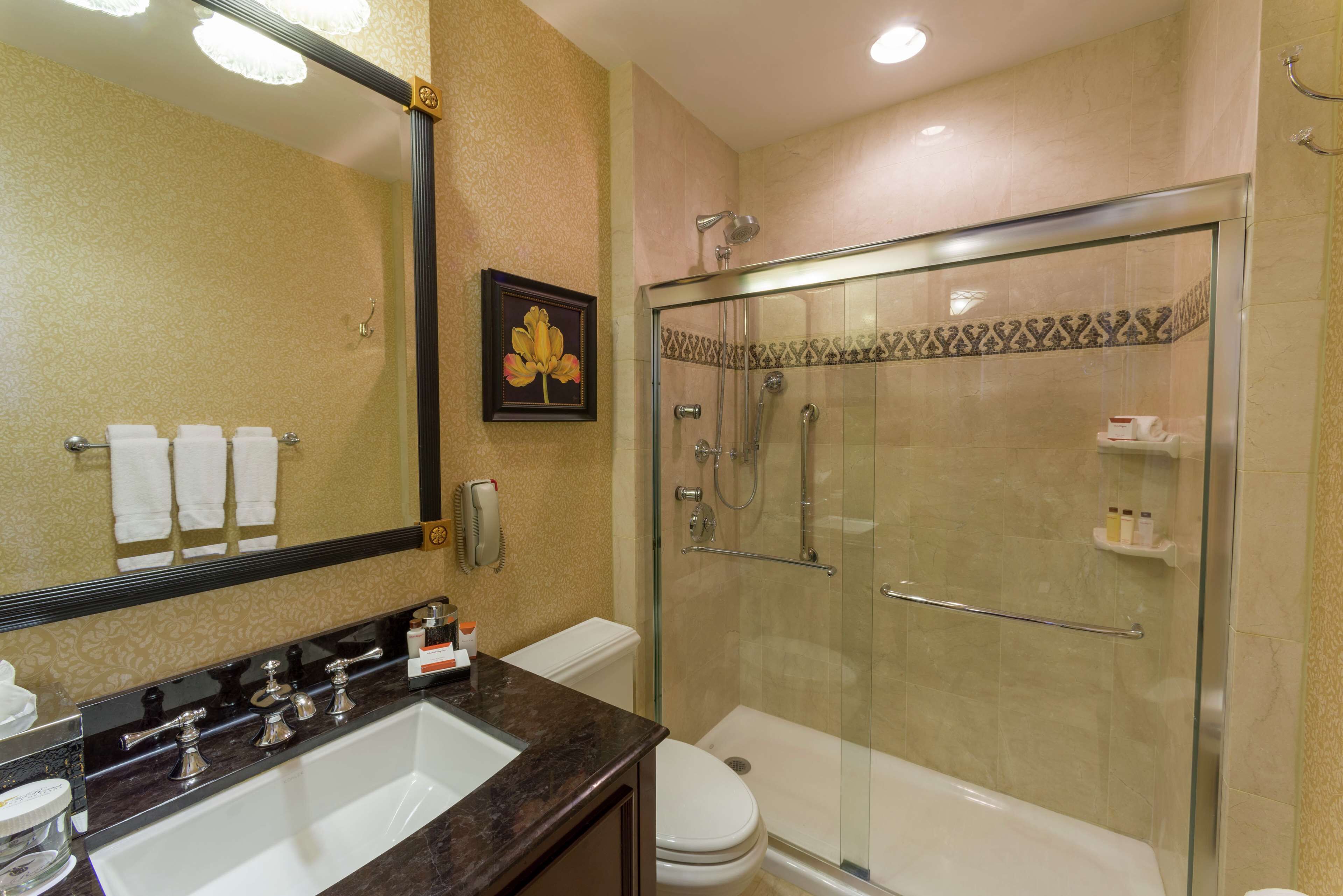 A bathroom with a large mirror, a sink, a toilet, and a glass-enclosed shower.