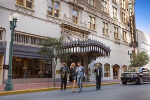 Un edificio histórico con arquitectura ornamentada, una entrada destacada y vista a la calle con un vehículo estacionado.