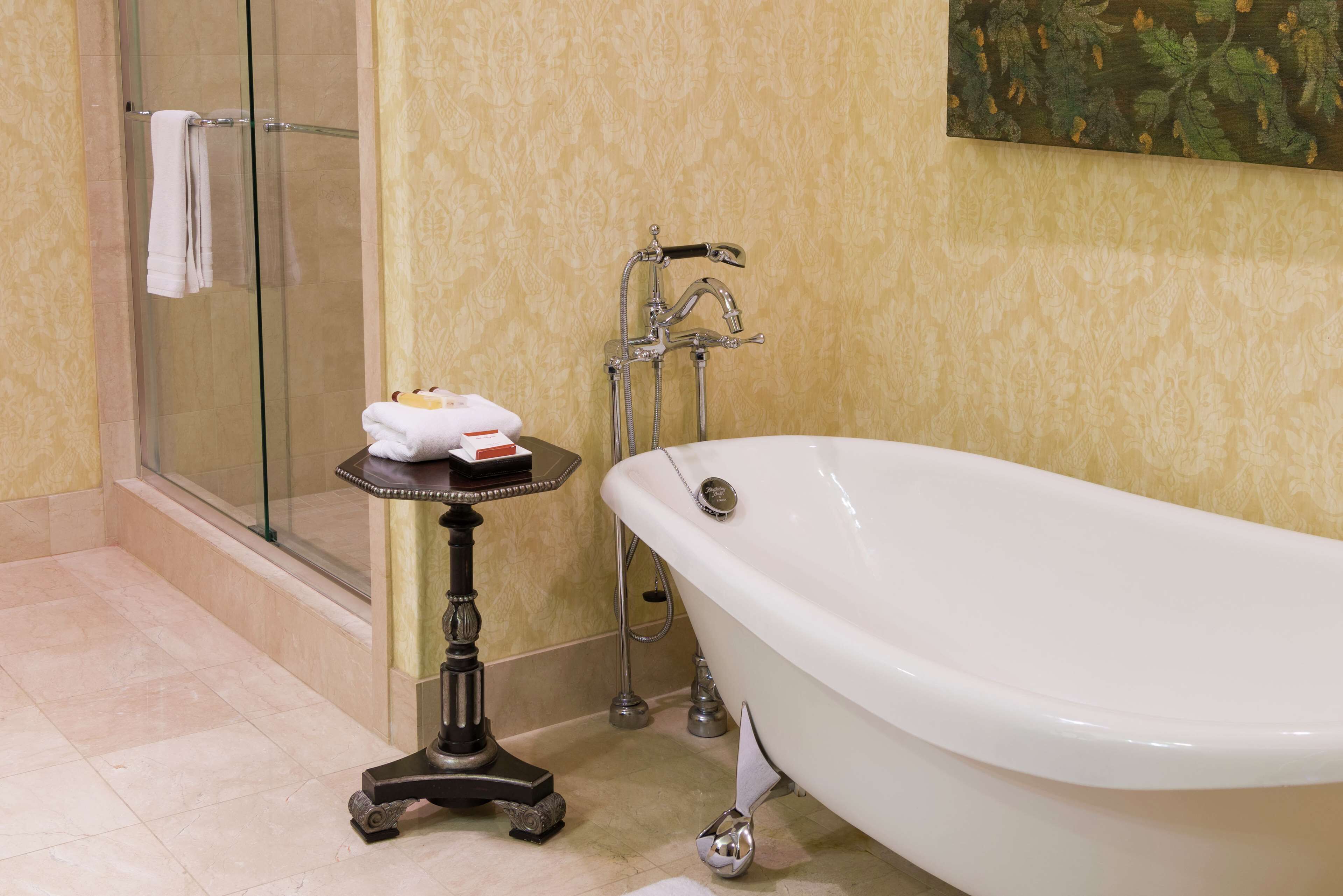 Un bagno con doccia vetro, vasca da bagno bianca e un tavolino con articoli da toilette.