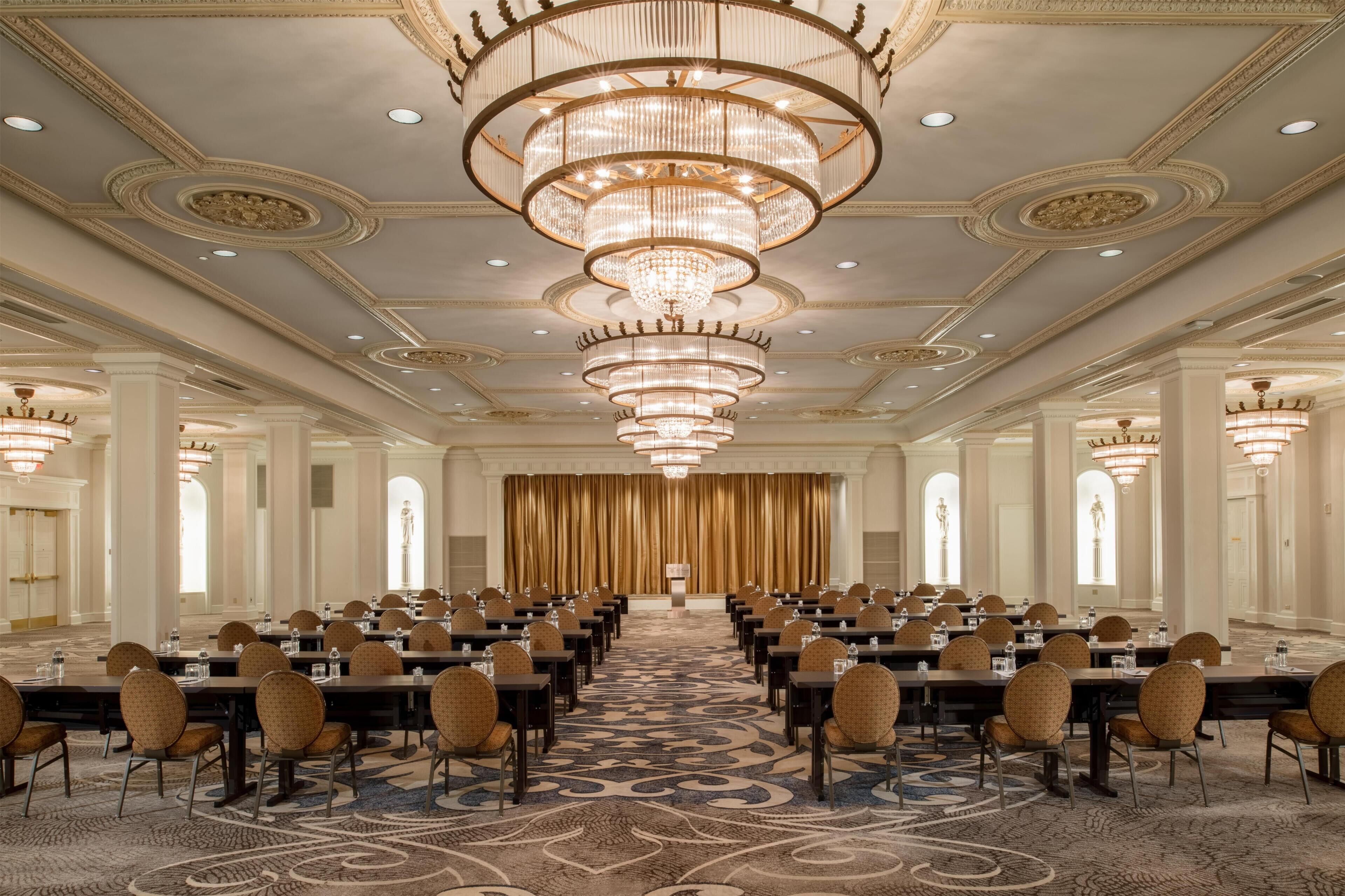 A conference room with rows of tables and chairs, a patterned carpet, and a large chandelier.