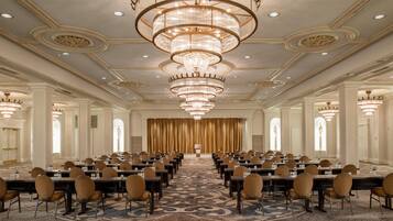 A conference room with rows of tables and chairs, a patterned carpet, and a large chandelier.