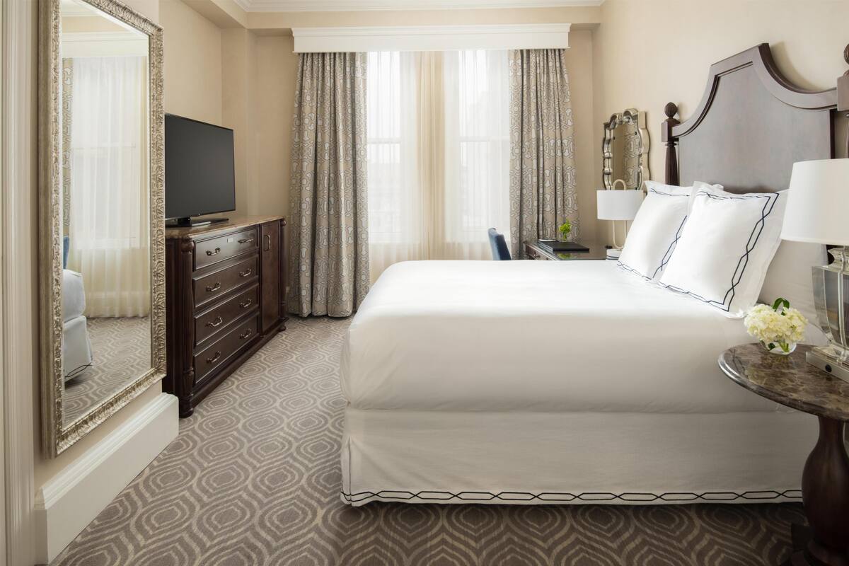 Een hotelkamer met een groot bed, een kaptafel, een televisie, een bureau met een lamp en een spiegel.
