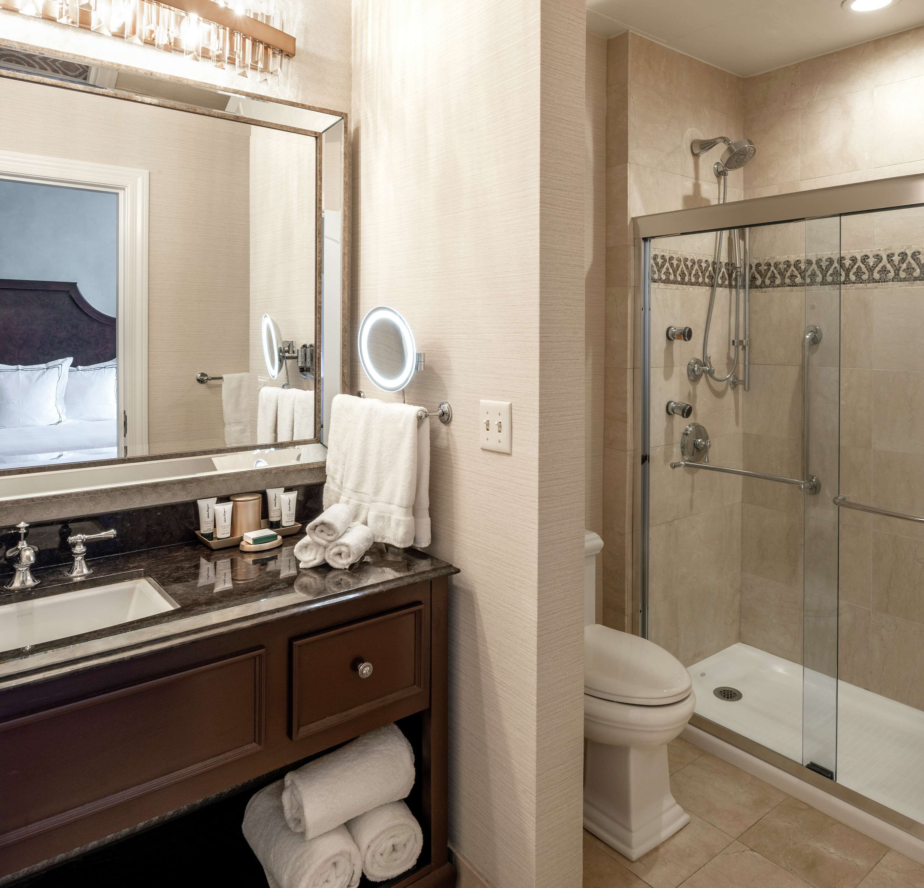 A modern bathroom with a large mirror, a sink with multiple faucets, a toilet, and a glass-enclosed shower.